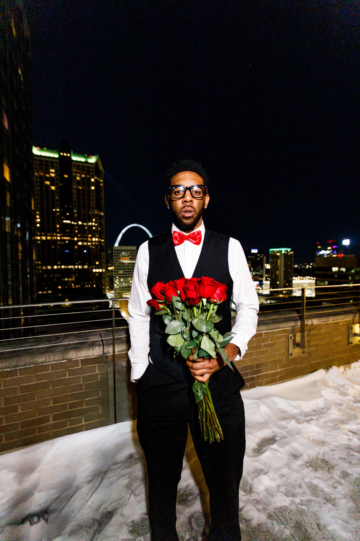 Dobbs on a St. Louis rooftop with the Gateway Arch, holding a bouquet of red roses